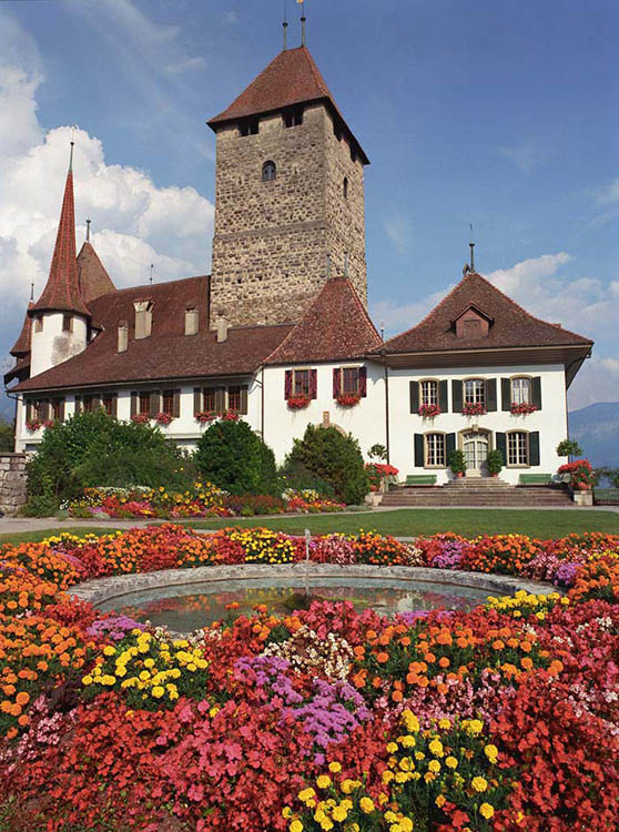 A flower garden and a pond have a small castle behind in Spiez SUI