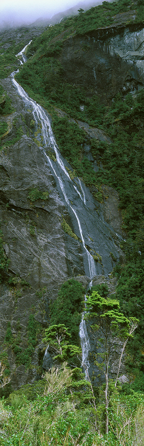 A small stream appears to flow from a cloud and flow over many rock faces near Milford Sound, NZ