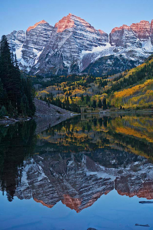 Sunrise at Maroon Bells with a near perfect reflection of the mountains and golden autumn foliage